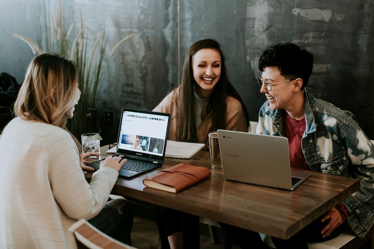 Three colleagues laughing together over laptops.